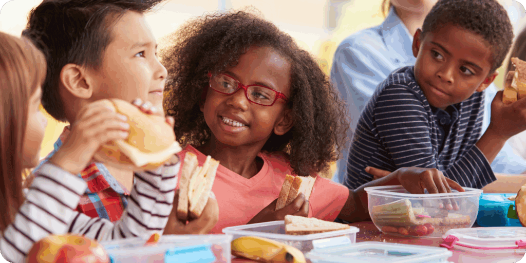 young children smiling and eating lunch at school
